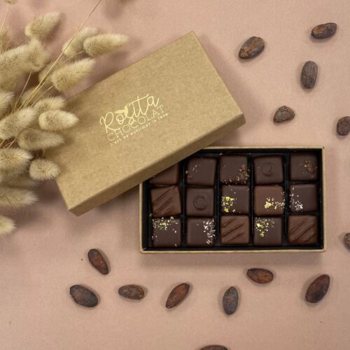 Photo d'ambiance d'un coffret de 15 pralinés aux 6 saveurs ouvert avec des fèves de cacao disposées autour