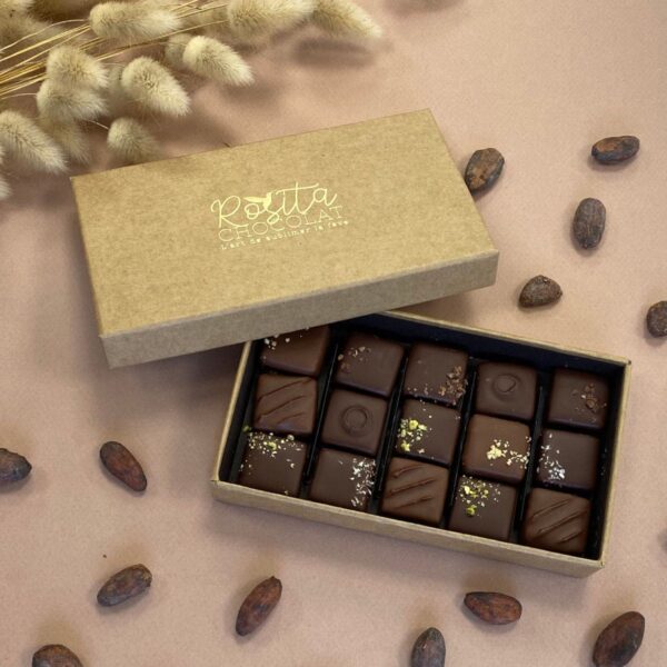 Photo d'ambiance d'un coffret de 15 pralinés aux 6 saveurs ouvert avec des fèves de cacao disposées autour