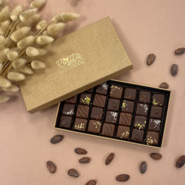 Photo d'ambiance d'un coffret de 28 pralinés aux 6 saveurs ouvert avec des fèves de cacao disposées autour